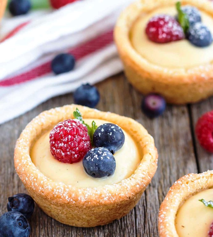 Bite-sized sugar cookie cups filled with a vanilla custard and topped with fresh berries.