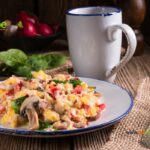 Scrambled Eggs Tomatoes and Spinach recipe for breakfast. Healthy fluffy scrambled eggs in a pan on the stove top, with vegetables on toast.