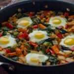 Healthy Breakfast Sweet Potato Hash recipe. Sweet potato, bell pepper, spinach vegetables with eggs in a pan for a vegetarian breakfast dish.