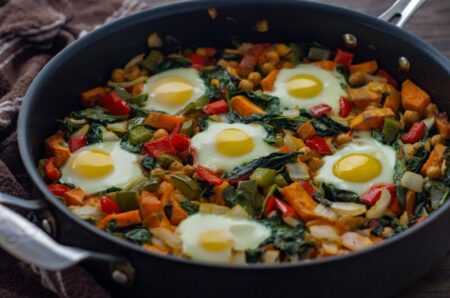 Healthy Breakfast Sweet Potato Hash recipe. Sweet potato, bell pepper, spinach vegetables with eggs in a pan for a vegetarian breakfast dish.