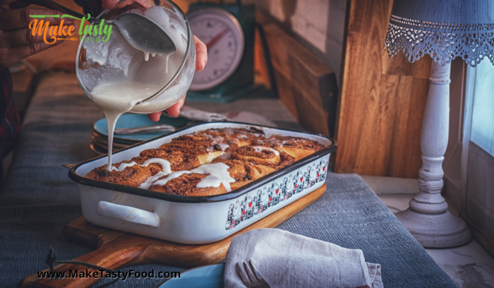 a casserole dish with cinnamon rolls being iced when they are warm. on a table