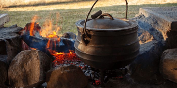 Filling Lamb Shank Potjie Pot. A South African family pot around the fire with lamb shank and potatoes. Simmering on coals while chatting.