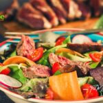 A delicious spicy steak salad lunch recipe for summer. Healthy bowl of veggies and cherry tomatoes on a lettuce, baby spinach bed and a simple dressings.