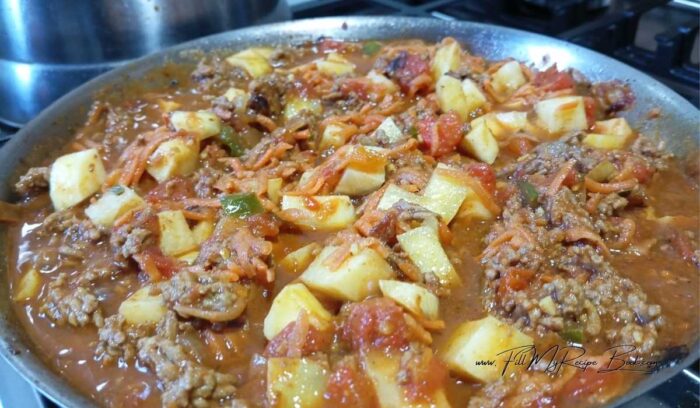 Pour in the water and apple cider vinegar and the jam and mix this together with the meat.
Add the grated carrots and the potato pieces or cubes. Then stir and mix them into this meat mixture.
