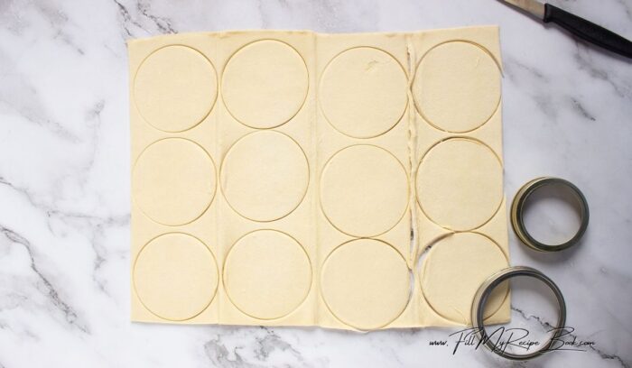 Roll out puff pastry slightly on a lightly floured surface. Cut out rounds using a 2.5–3 inch cookie or biscuit cutter. Cut half of those rounds again with a smaller cutter (like 1.5 inches) to create rings.