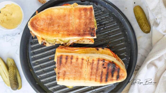 Cut the Cuban bread in half lengthwise and spread mustard on both sides.
Layer the  roast pork, ham, cheese and pickles on one half of the bread.
Place the other half of the bread on top and press down gently.
Heat a large skillet or panini press over medium heat.