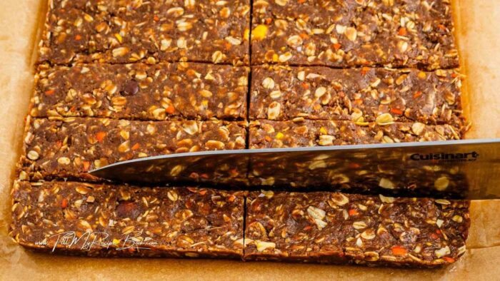 Press the mixture evenly into the lined 8x8 pan.
Cover with foil or plastic wrap and chill until set. (Place in freezer for at least 30 minutes or place in refrigerator for at least 60 minutes).
Remove pan from freezer, and lift out the frozen “block” of bars by grabbing the parchment/wax paper liner and lifting it out of the pan.
Cut the frozen “block” into 12 bars.