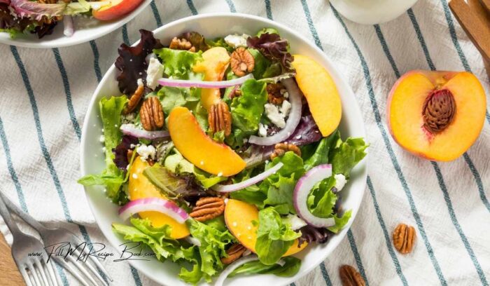 Add some of the dressing to the lettuce leaves, and toss in the fresh sliced ripe peaches and onion slices, feta crumbs and pecan nuts. Add the remainder of the dressing to this tossed salad and serve.