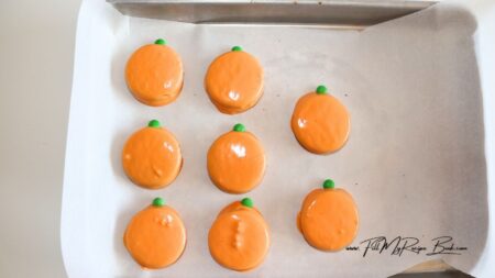 Place parchment paper onto cookie sheet, set aside. Place orange melting chocolate into microwave safe bowl, melting in 30 second increments, stirring after each.
Once melted complete cover cookie in chocolate, shaking off any excess. Place on prepared cookie sheet.
Place a mini M & M's at the top to be the stem.