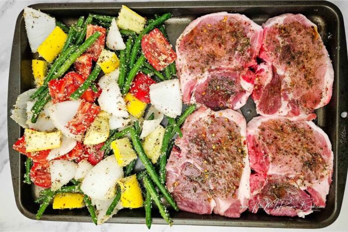 Cut the vegetables and place them into a large bowl.
In a small bowl, mix together the oil and seasonings. Pour half of it over the vegetables along with the grated Parmesan cheese and toss. Set aside.
Pound the pork chops to tenderize, then brush the remaining seasoning mixture over both sides to coat. Arrange the one one half of the sheet pan.
Spread the vegetables evenly on the other side of the sheet pan.
Transfer the baking sheet to the oven. Bake for 8 minutes, then flip the pork chops and bake for an additional 8 minutes.