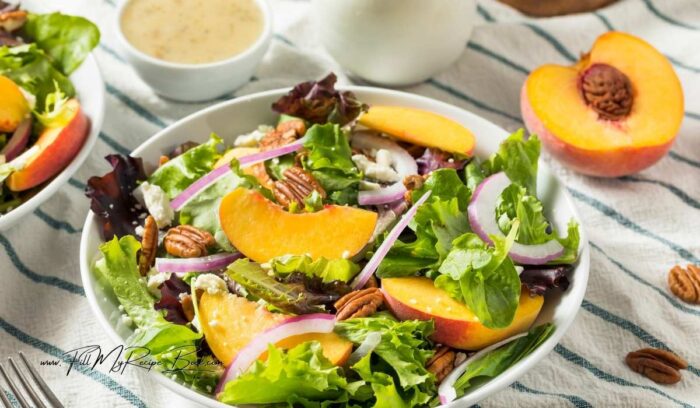 A quick homemade fresh peach salad recipe with feta and pecan nuts on a lettuce bed, drizzled with a simple honey dressing. a healthy summer side dish.
