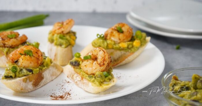 First defrost the shrimp.
Then add a little olive oil to a sauté pan over medium-high heat.
Add in the defrosted shrimp, salt, pepper, and chili powder.
Mix to combine and cook until shrimp turn pink.
While the shrimp are cooking, turn the oven or broiler on.
Add the sliced baguette to a baking sheet and toast for a few minutes,
Remove from the oven, and carefully add a large spoonful of guacamole to each toast.