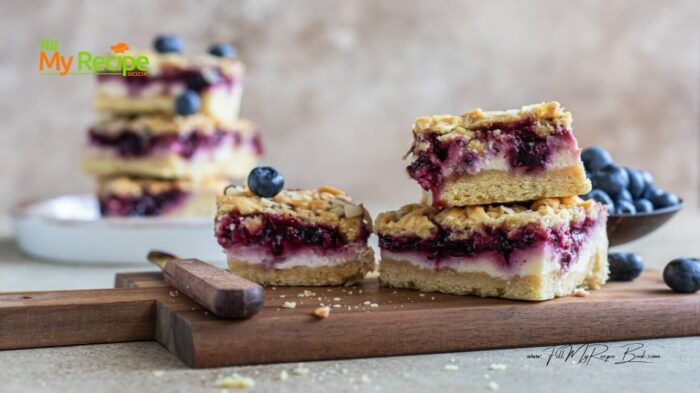 Baked Homemade Blueberry Crumble Cheesecake Bars, buttery shortbread base, cheesecake, juicy blueberry layers, with crumbed almond topping.